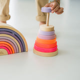 Kind stapelt großen Scheibenturm aus Naturholz von Grimm's in Neonpink