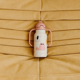 Kimmie Kinder-Trinkflasche von Liewood im Design "Cats and Dogs" auf Sofa liegend