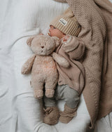 Baby im Bett mit Moonie Teddybär Einschlafhilfe und Kuscheltier im Farbton Organic Sand