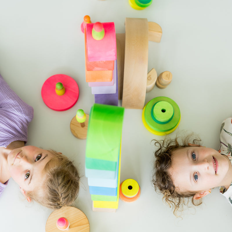 Zwei Kinder liegen auf Boden mit Holzspielzeug von Grimm's in Neonfarben