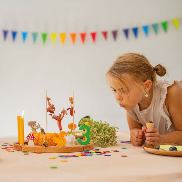 Kind an Geburtstagstisch mit Grimm's Wimpelkette aus Holz in Regenbogenfarben