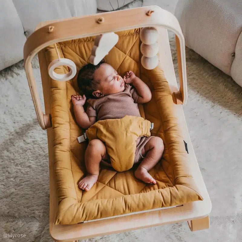 Kind in Charlie Crane Levo Babywippe aus Buche mit Camel-Bezug