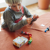 Kind fädelt bunte Holzteile aus dem Grapat Adventskalender 2026 auf eine Schnur