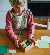 Kind sortiert kleine Spielschätze aus dem Grapat Adventskalender 2026 in einer Box