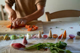 Kind schneidet Gemüse mit handgemaltem Holzgemüse "Veggies" von Grapat im Vordergrund