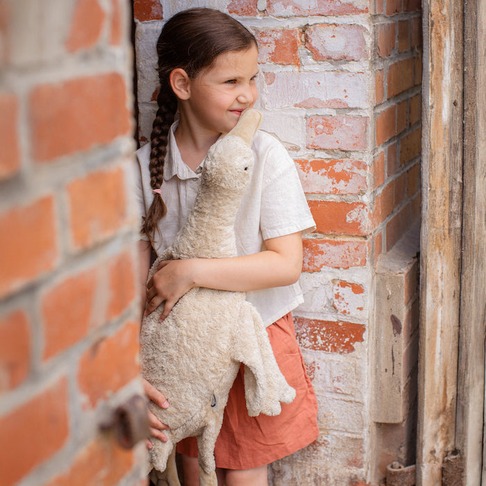 Kind vor Ziegelwand stehend mit großer Gans im Farbton Leinen von Senger Naturwelt