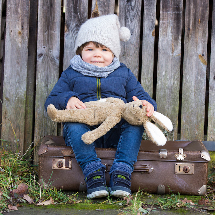 Kind sitzt auf Koffer und hält Schlenker Kuscheltier Großer Hase in Beige von Senger Naturwelt