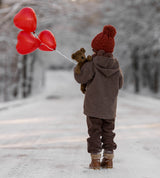 Kind mit Braunem Bär Schlenker Kuscheltier von Senger Naturwelt sowie roten Luftballons