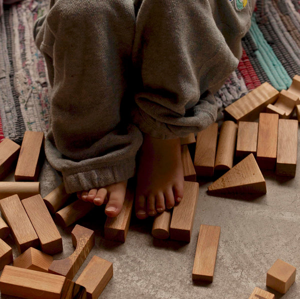 Kinderfüße auf 30 naturfarbene Holz-Bauklötze von Wooden Story